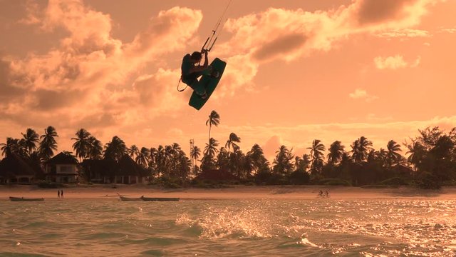 SLOW MOTION: Extreme kiteboarder jumping high at golden orange sunset