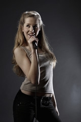 Beautiful teenage girl singing into microphone on gray background