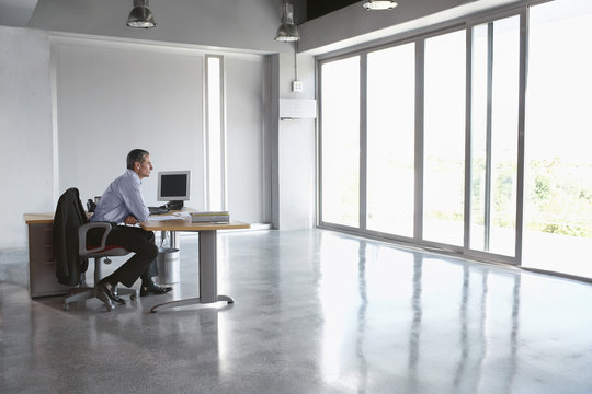 Full Length Side View Of A Man Sitting At Desk In Empty Office