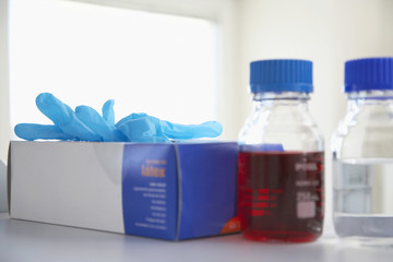 Closeup of a box of rubber gloves next to chemical bottles on shelf