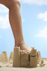 Low section of girl's leg stepping on sand castle at beach