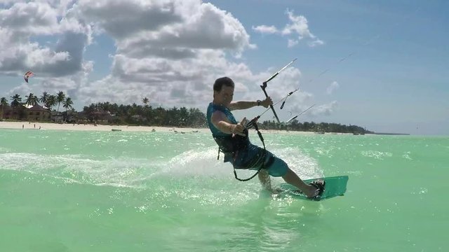 SLOW MOTION: kiter kiteboarding past the camera showing shaka surf sign