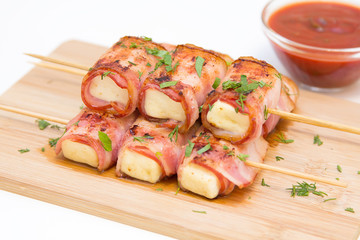 Rolls of feta cheese in bacon with spicy tomato sauce, selective focus