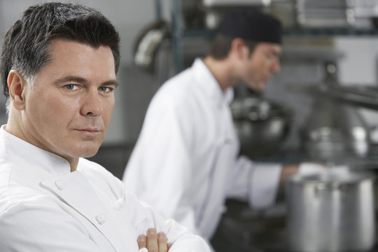 Closeup of a serious chef with blurred colleague in the background in kitchen