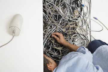 Cropped man working on tangled computer wires in office