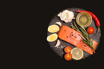 Fillet of salmon, tomato and herbs over on black stone slate.