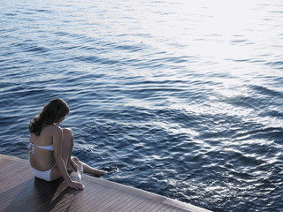 Rear view of woman dipping foot in sea while sitting on yacht's floorboard