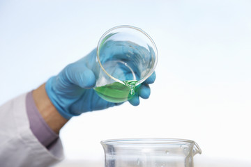 Closeup of gloved hand pouring green liquid into beaker against blurred background