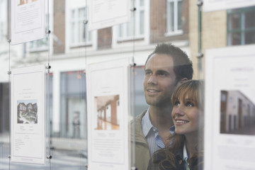 Closeup of a young couple looking through window at estate agents