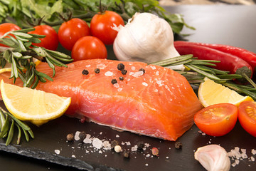 Fillet of salmon, tomato and herbs over on black stone slate.