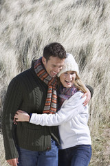Cheerful couple in winter clothing embracing in long grass