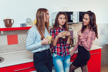 Beautiful girls standing in kitchen at the hostel talking and drinking tea.