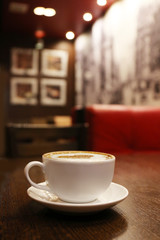 Cup with hot tasty coffee on wooden table in cafe, close up view