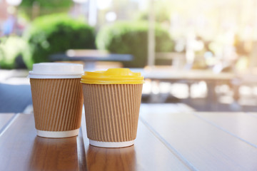 Two paper cups with tasty hot coffee on wooden table outdoors