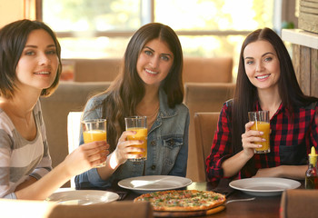 Cheerful young women sitting in cafe with pizza and juice