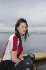 Side view of thoughtful young woman with surfboard looking away while sitting on beach