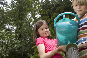 Low angle view of a young boy and girl watering flowers in garden