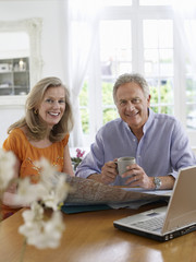 Portrait of a mature couple with map and laptop sitting at dining table in home