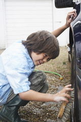 Side view of a boy washing car wheel with a brush