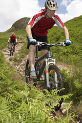 Obraz na płótnie Canvas Two cyclists on countryside track against hill and sky