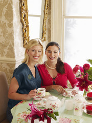 Portrait of two smiling young women having tea at dining table