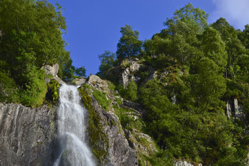 The edge of a tropical waterfall with blue sky and foliage surrounding, Aber falls abergwyngregyn wales