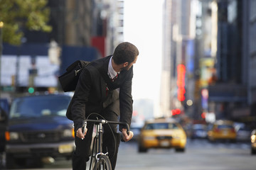 Young businessman looking over shoulder while riding bicycle on urban street