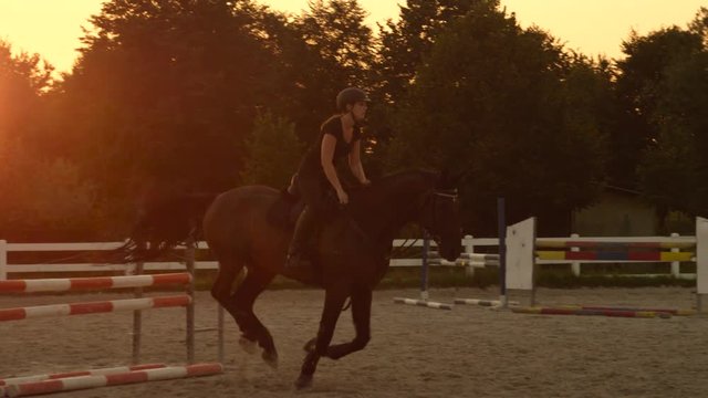 SLOW MOTION: Female rider training showjumping in equestrian center at sunset