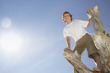 Low angle portrait of happy young boy climbing on dead tree trunk