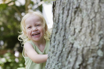 Portrait of a cheerful little girl peeking from behind tree