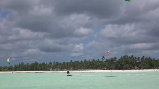 Female kiteboarder kiting in perfect blue lagoon in front of exotic sandy beach
