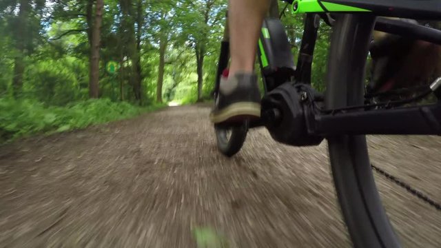 CLOSE UP: Biker riding and pedaling electric bike on gravel dirt road in forest