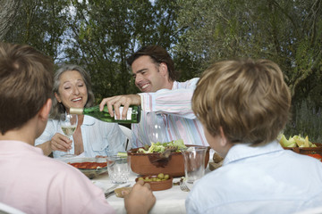 Family with children dining in garden as man pours wine into glass