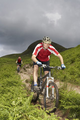Fototapeta premium Two cyclists on countryside track against hill and sky