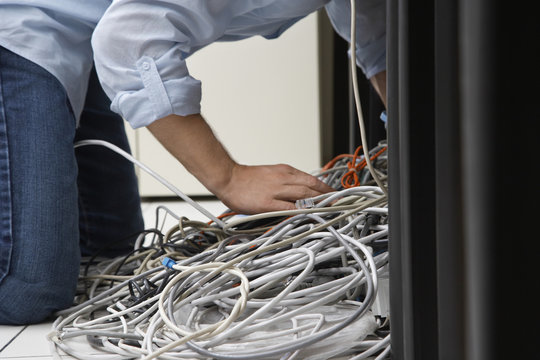 Side View Of A Man Working On Tangled Computer Wires In Office