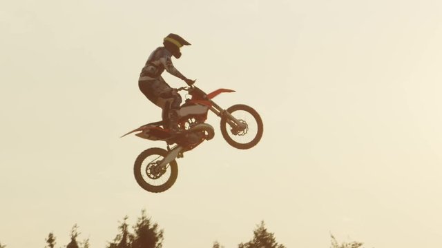 SLOW MOTION: Freestyle motocross biker jumping superman trick over sunset sun