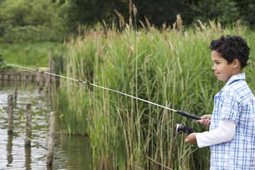 Side view of happy young boy fishing in lake