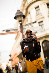 Naklejka premium Young african american woman walking through the city with coffe