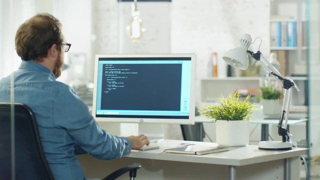 Young Bearded Developer Writes Code on His Desktop Computer. He Works in a Modern Office.  Shot on RED Cinema Camera in 4K (UHD).