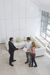 Elevated view of a male real estate agent shaking hands with a man by woman in new home