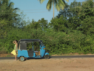 Full length side view of a young woman leaning on old fashioned auto rickshaw on dirt road