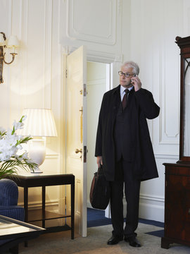 Full Length Portrait Of A Middle Aged Businessman Using Mobile Phone With Briefcase In Living Room