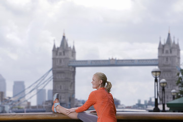 Smiling young blond woman stretching in front of Tower Bridge in England