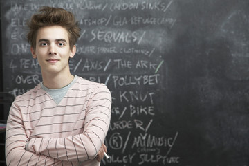 Portrait of happy young man standing in front of blackboard