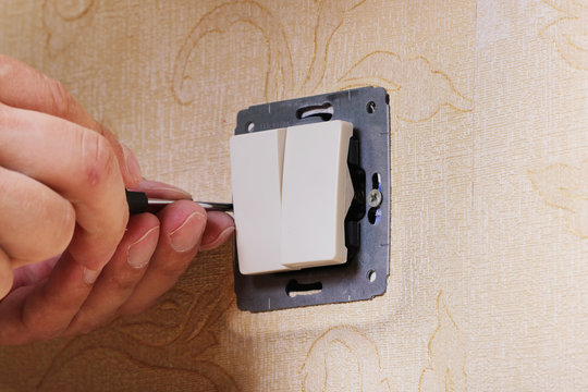 Worker man electrician is repairing damaged switch in the apartment, installation of new closeup