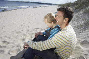 Side view of happy father and daughter sitting on sandy beach