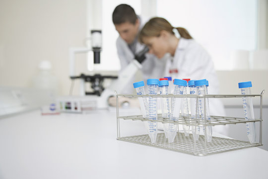 Side view of scientists looking in microscope with test tubes in focus at laboratory