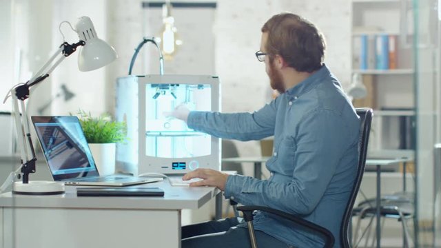 Young Bearded Developer Uses 3D Printer for Modeling. He is Sitting at His Desk in a Technologically Modern Office.  Shot on RED Cinema Camera in 4K (UHD).