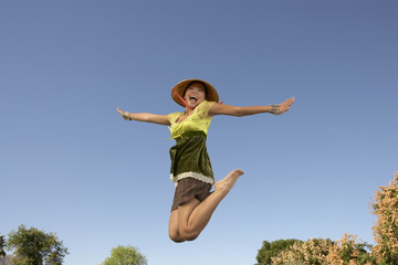 Obraz premium Cheerful Asian woman jumping with arms outstretched against blue sky
