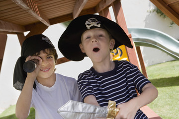 Little boy wearing pirate hat with friend looking through telescope
